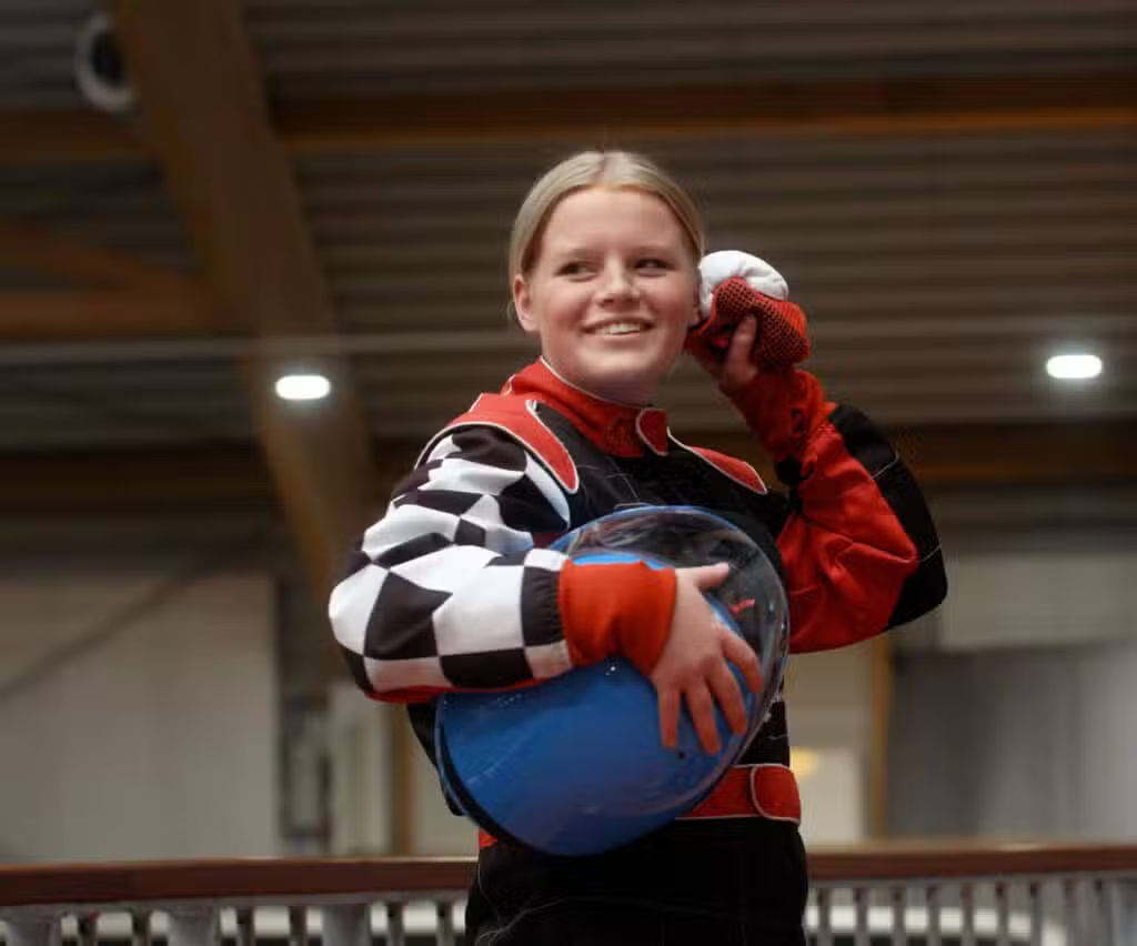 Ung pige i racingdragt, smilende med hjelm i hånden