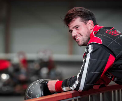 En racerkører iført en racerkøredragt og hjelm, som smiler.