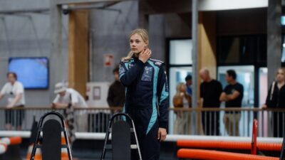 Alba Hurup Larsen Ung kvinde, ung racerkører i racerkøredragt står ved en gokart racerbane.